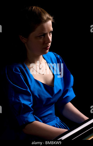 beautiful girl in blue dress playing the grand piano, isolated on black Stock Photo