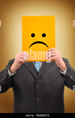 Businessman in gray suite is holding a yellow folder with sad face drawn on it Stock Photo