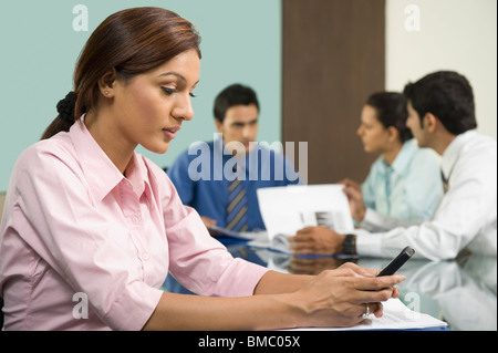 Businesswoman using a mobile phone with her colleagues working behind her Stock Photo