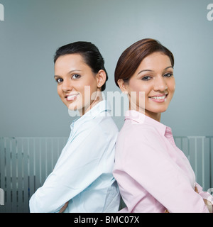 Two businesswomen standing back to back and smiling Stock Photo
