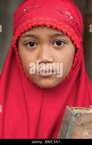 Young muslim girl wearing red veil while holding Quran, East Java, Indonesia Stock Photo