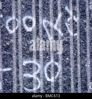 Surface markings on a textured gray wall reveal numerical symbols indicating measurements or references Stock Photo