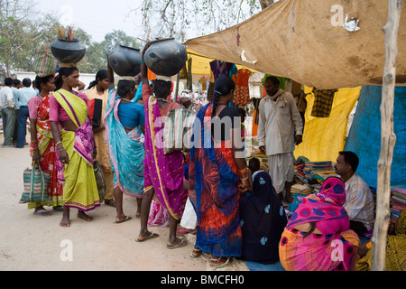 Asian Women shopping in rural India village marketplace dressed in bright colorful saris carry purchases in pots on their heads Stock Photo