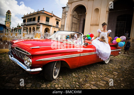 Fourteen-year-old girl sits on a vintage car as she poses for a photo on the day of her Quinceanera party in Trinidad, Cuba Stock Photo