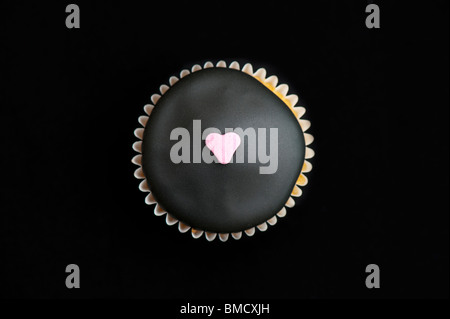 Mini cupcake decorated with black icing and a sugar heart on a black background Stock Photo