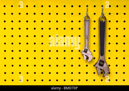Pair of metal wrenches hang together off of hooks on yellow pegboard. Stock Photo