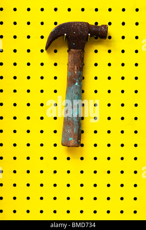 Old hammer with paint marks hangs from metal hook. Wooden handle with metal head. Stock Photo