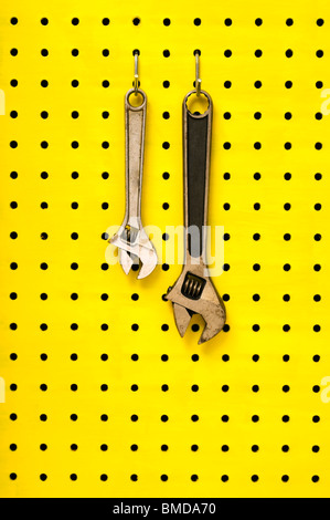 Pair of metal wrenches (spanners) hang together off of hooks on yellow pegboard. Stock Photo