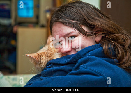 Thirteen year old brunette teenager wearing denim jacket holding ginger colored cat looking over her left shoulder at camera Stock Photo