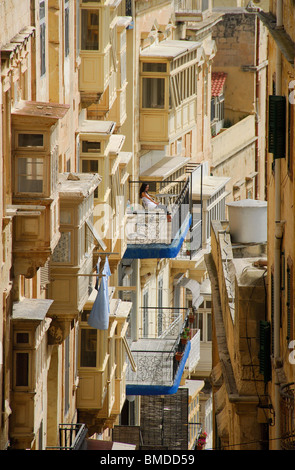 VALLETTA, MALTA. A young woman sitting on a hotel balcony on Triq il-Batterija and looking out over the Grand Harbour. Stock Photo