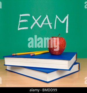 Exam written on a chalkboard. Books, pencils and an apple on foreground. Stock Photo