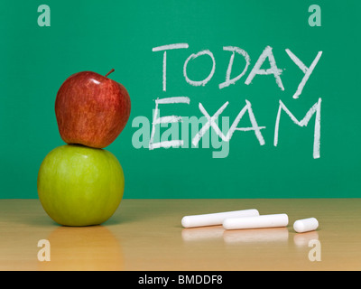Today exam written on a chalkboard. Some chalks and apples on the foreground. Stock Photo