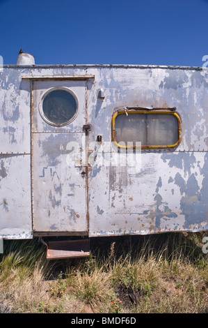 A frequent sight in New Mexico - a dented, paint-peeling, derelict camping trailer sitting in a weed-patch - Encino, New Mexico. Stock Photo