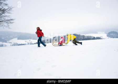 Mother Pulling Daughter in Sled, Son Pushing Sled from Behind Stock Photo