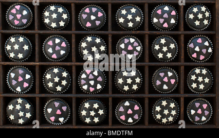 Mini cupcakes decorated with black icing, sugar hearts and white chocolate stars in a wooden tray Stock Photo