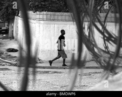 A man walks along a street in Port au Prince, Haiti, behind coils of razor wire Stock Photo