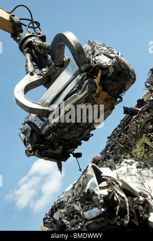 A scrap car being lifted by grab crane on to a pile of other scrapped cars. Stock Photo