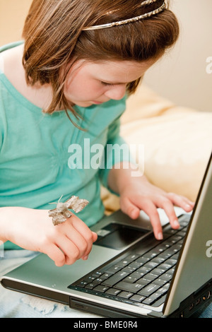 Young girl holding a poplar hawk moth and researching moths on a laptop in her lounge Stock Photo