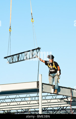 a steelworker guides a beam into position as part of the structural ...