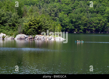 Eagle Lake in the Adirondack State Park. A canoe with three people approaching a rocky island. Stock Photo