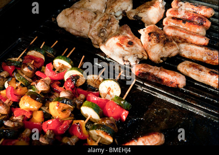 Sausages, chicken and vegetable kebabs being cooked together on a barbecue. Stock Photo