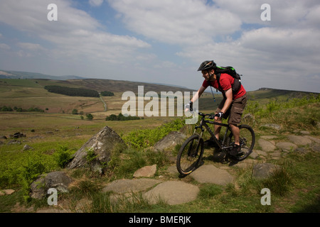 Cyclist descends footpath suffering from erosion beneath Stanage Edge gritstone cliffs, Peak District National Park, Derbyshire. Stock Photo