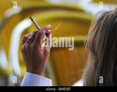 A woman holds a cigarette and a crisp in a cafe in St Mark's Square, Venice, italy Stock Photo