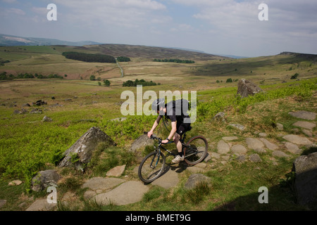 Cyclist descends footpath suffering from erosion beneath Stanage Edge gritstone cliffs, Peak District National Park, Derbyshire. Stock Photo