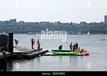 people launching colorful kayaks from floating launch platform on Hudson River waterfront in Hells Kitchen New York City Stock Photo