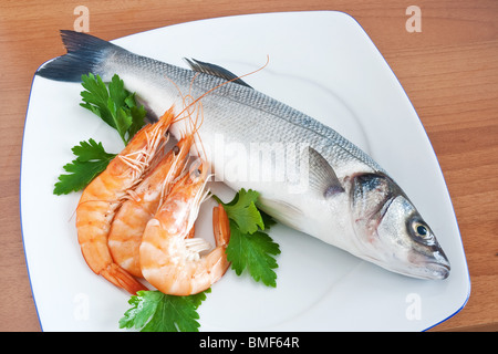 plate with sea bass, prawns, and parsley isolated on wooden background Stock Photo