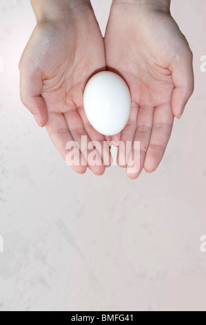 A conceptual image of a young woman's hands holding an egg against a beige background. Concept fertility, concept reproduction. Stock Photo