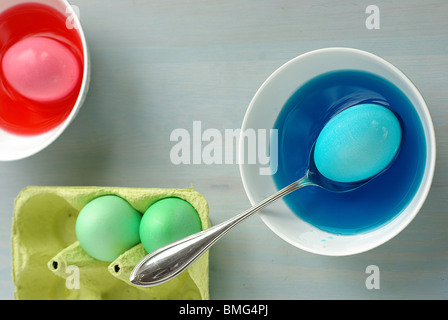 Easter Eggs being dyed in several bowls of brightly coloured dye, Vertical Stock Photo