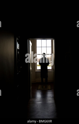 Man in overcoat standing looking out of window Stock Photo