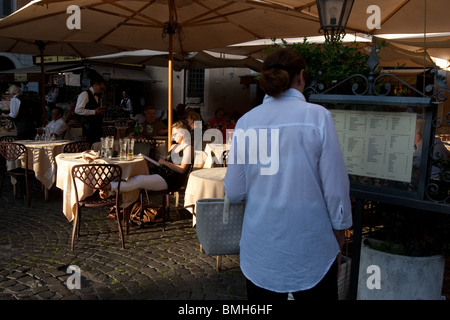 young woman tourist read a book in a touristic outdoor Bar in Santa Maria in Trastevere square Rome Italy scene. Stock Photo