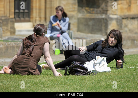 Two young English women sit on the grass enjoy smoking cigarettes outside in a public place during their lunch break Stock Photo