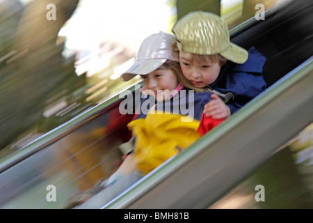 young boy and his little sister going down a slide Stock Photo