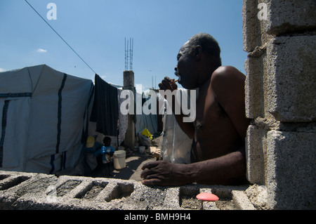 An earthquake survivor brushing his teeth next to tents made of sheets at a temporary makeshift dwelling Port au Prince, Haiti Stock Photo