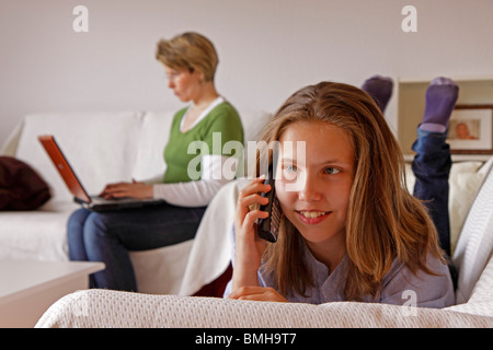 a mother trying to work on her computer while her daughter is talking on the phone beside her Stock Photo