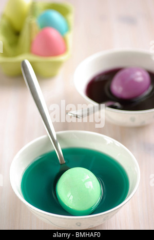 Easter Eggs being dyed in several bowls of brightly coloured dye Stock Photo