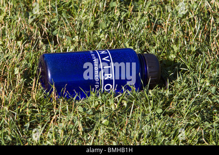 A empty blue plastic water bottle from an environmental company laying in the grass. Stock Photo