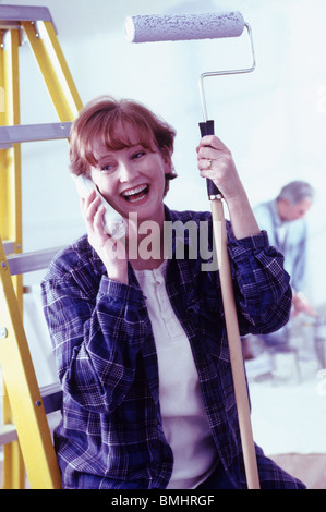 Woman talking on phone while holding a paint roller Stock Photo