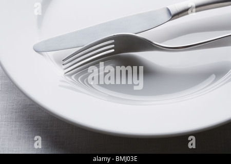 Fork and knife on empty white plate Stock Photo