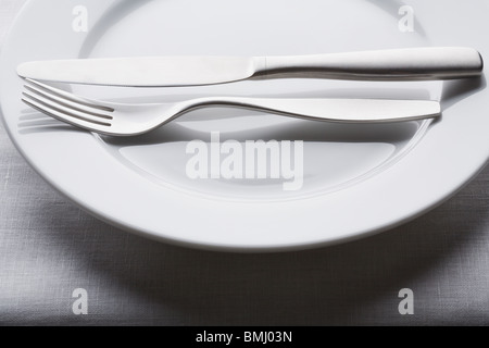 Fork and knife on empty white plate Stock Photo