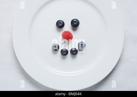 Smiley face of blueberries and raspberry on white plate Stock Photo