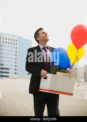 Businessman holding box and balloons Stock Photo