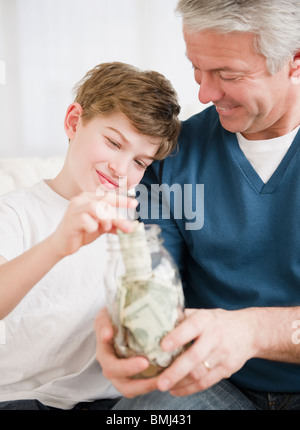 Father and son putting money in jar Stock Photo