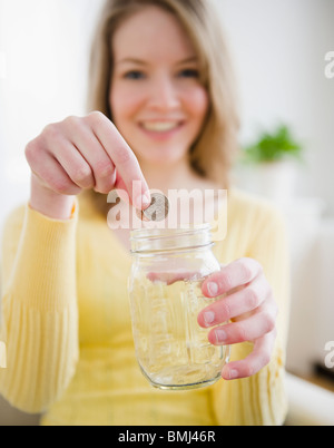 Woman putting coins in a jar Stock Photo