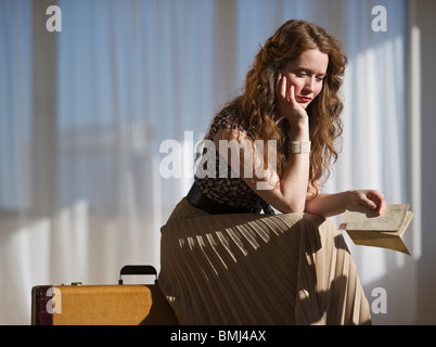 Somber woman sitting on suitcase Stock Photo