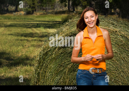 Smiling teenage girl beside a hay bale outside in a field. Stock Photo