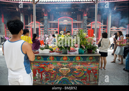 A visitor to the Longshan Temple in Taipei holds his hands in prayer by a painted altar laden with fruit and flowers. Stock Photo